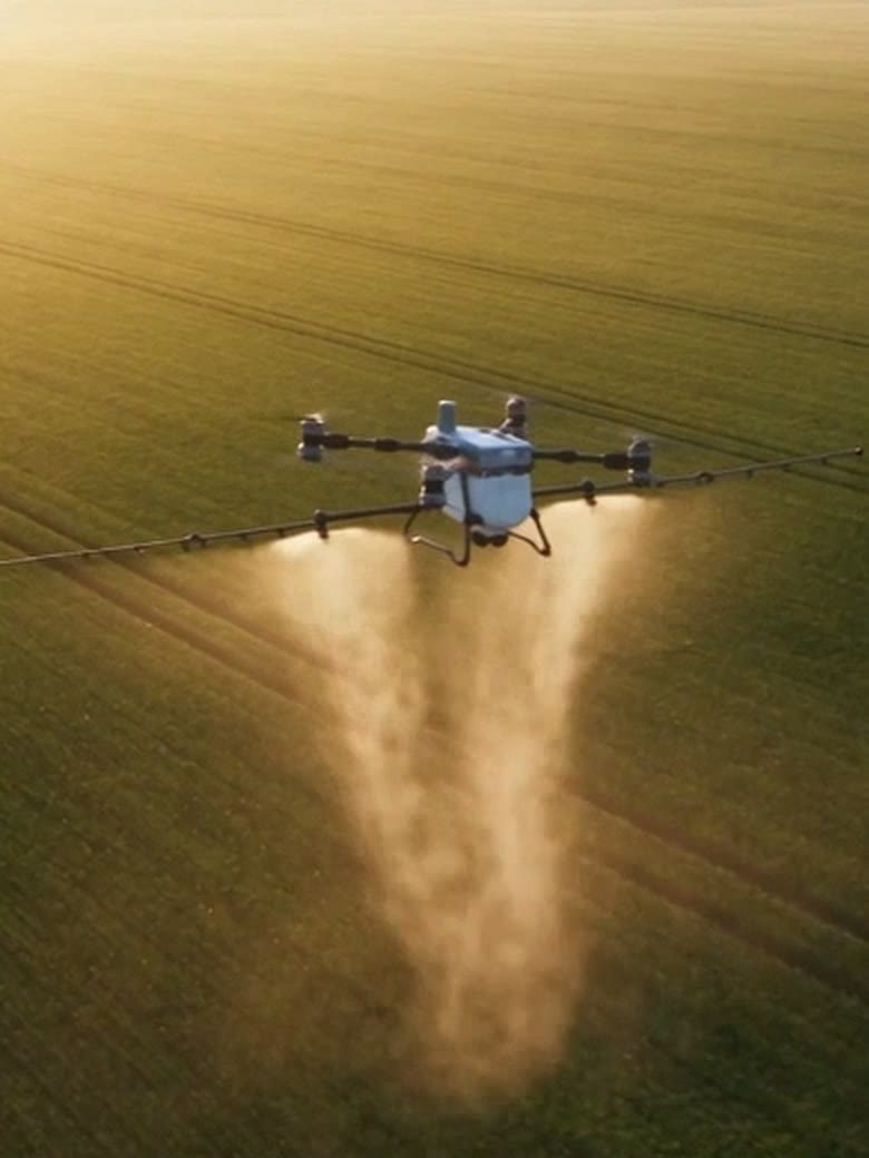 An agricultural drone flying low over the crop, spraying from its nozzles