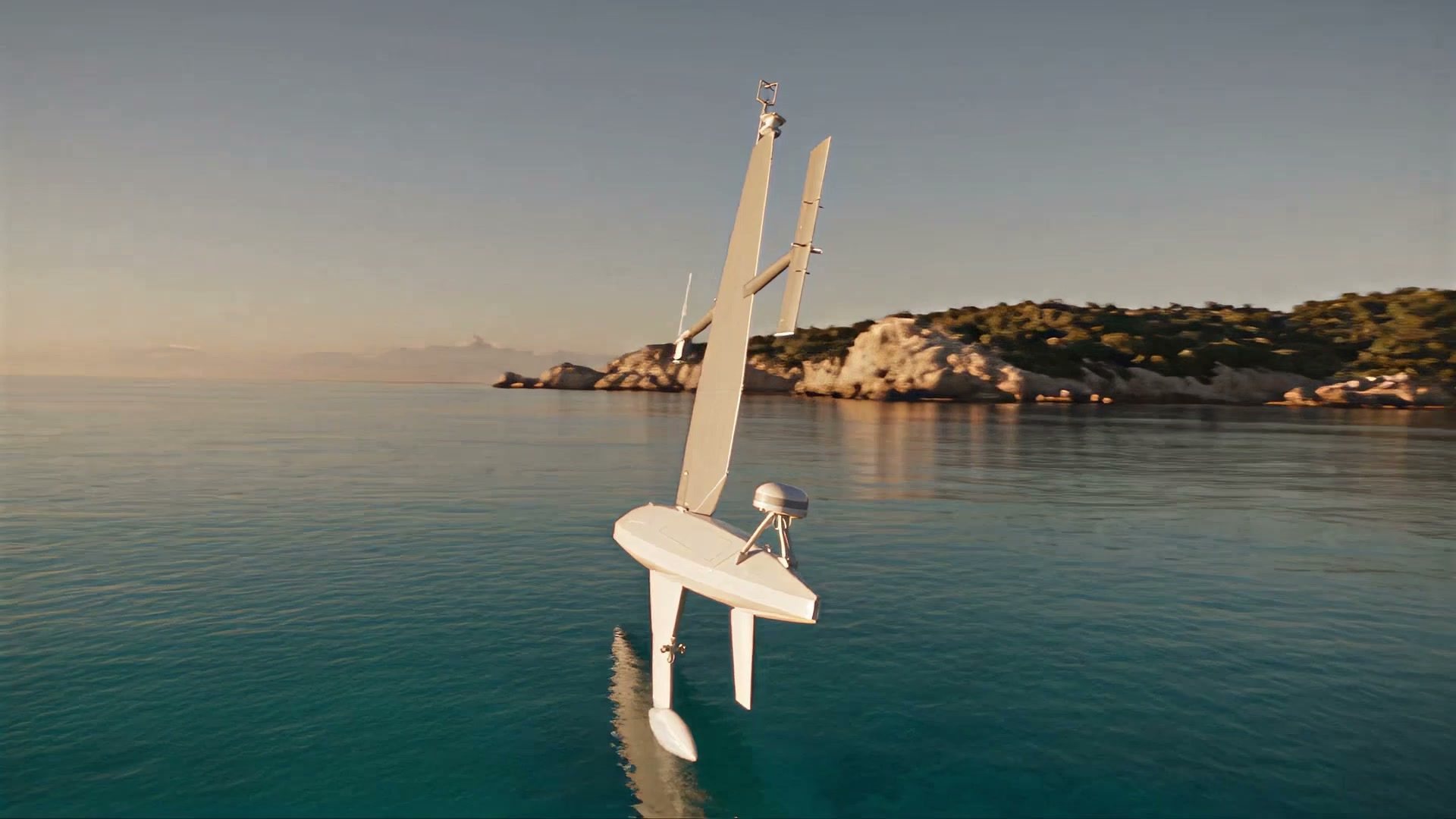 A sailing drone below a granite coast in low light, seen from the water