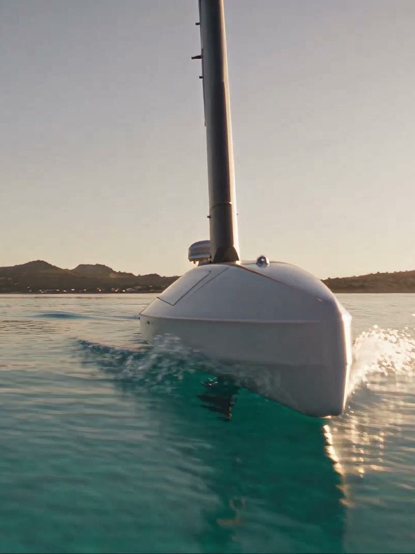A sailing drone below a granite coast in low light, seen from the water