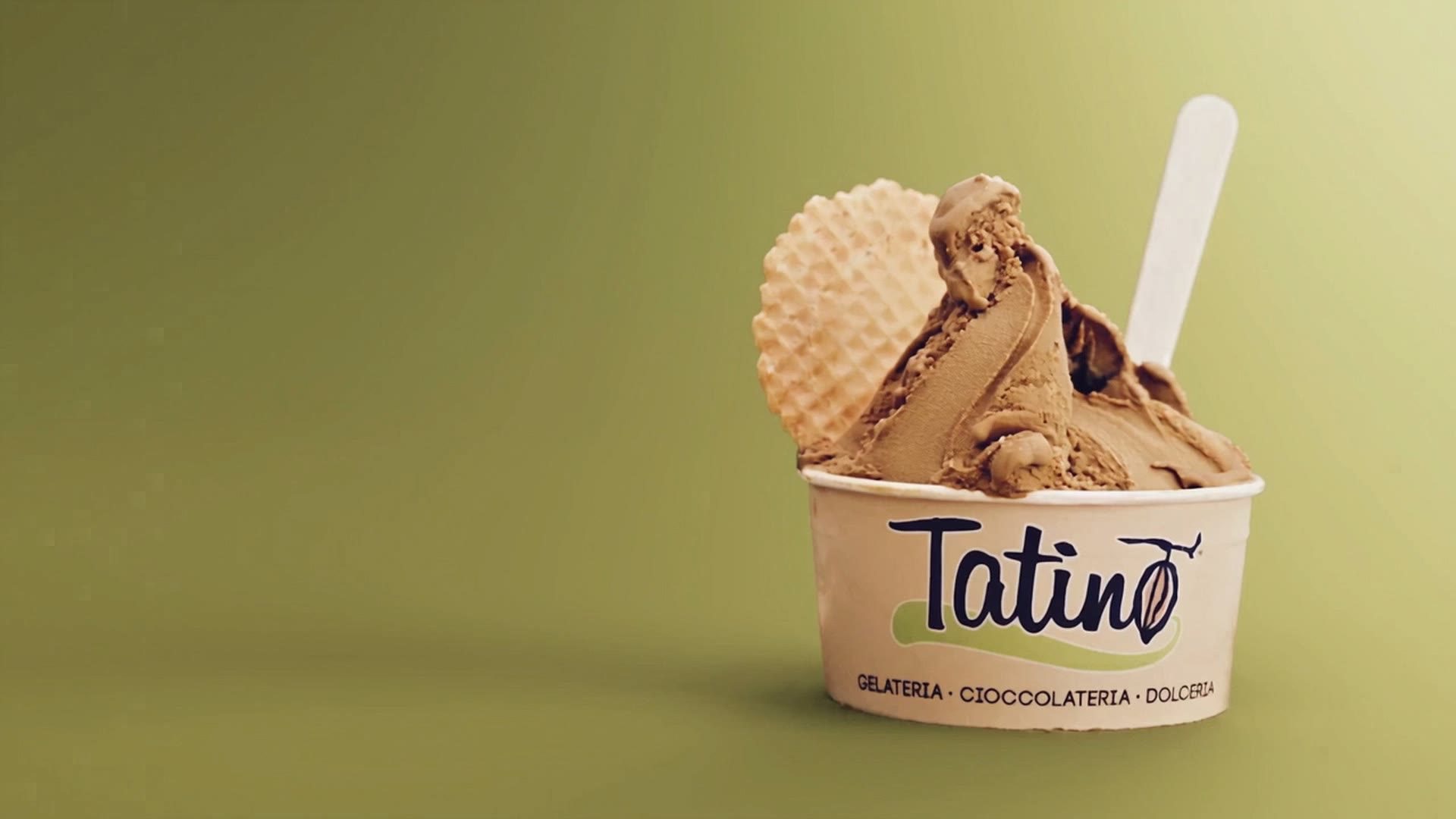 A Tatino cup of hazelnut gelato with a wafer, on an olive green background